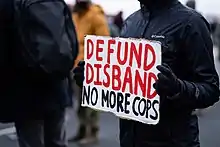 A protest sign with the words "defund / disband / no more cops"