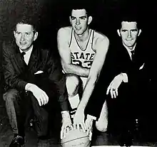 Head coach Babe McCarthy, captain Joe Dan Gold, and assistant coach Jerry Simmons each take a knee with their hands on a basketball.