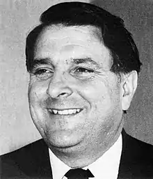 A black and white portrait of a smiling man wearing a suit and tie