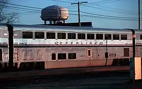 A stainless steel bilevel passenger rail car. A blue stripe and two thinner red stripes are on the side between the two levels of windos.