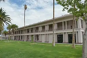 A two-story white hotel with a grass lawn surrounded by palm trees