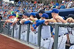 Men in white baseball uniforms leaning on a dugout railing