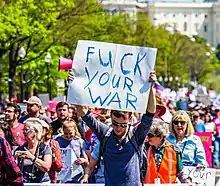 A protester holding a cardboard sign that reads "FUCK YOUR WAR"