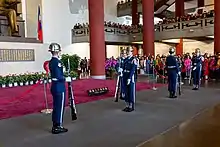 Five men in blue uniforms and silver hats performing a rifle drill