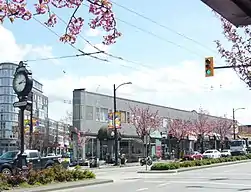 Street view of urban area with prominent clock, overhead tram wires, and modern buildings