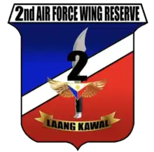 A shield-style crest primarily in red and blue, divided with a diagonal white bar.  The centre contains an symbolic military knife with the number '2' covering its blade.  The crest is headed by '2nd Air Force Wing Reserve' in all-upper-case letters.  Below the knife is a yellow banner for its motto containing the phrase 'Laang Kawal'.