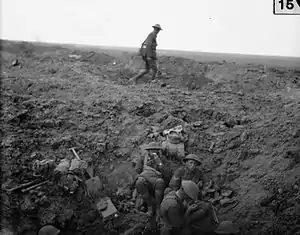 battlefield landscape with men resting in a shellhole in foreground