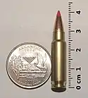 Photo of a 5.7×28mm SS196SR cartridge next to a quarter and ruler, in a size comparison.