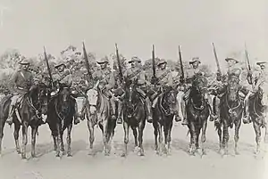 A group of eight soldiers wearing slouch hats with rifles raised into the air on horseback