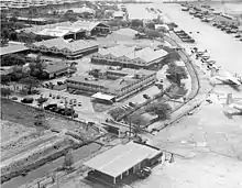 An aerial view of a compound consisting of several buildings, hangars, and small airplanes lining a runway