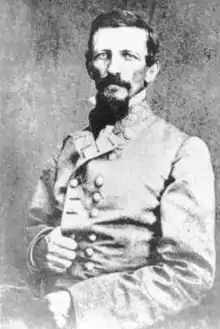 Black and white photo shows a man with moustache and beard. He wears a gray military uniform with two rows of buttons.