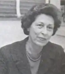 A middle-aged white woman with coiffed hair, wearing a dark suit jacket and a strand of beads