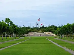 Grassy field leading up to a terraced site with five flags