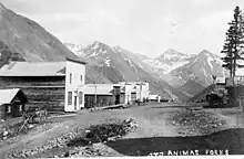 Wood buildings with false fronts line a rocky dirt street, 1880s.