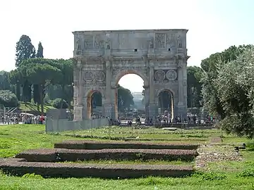 Landscape view of the Arch of Constantine across the Campus Martius with the via Sacra behind with trees and the Caelian Hill rising on the left and the Palatine Hill on the right.