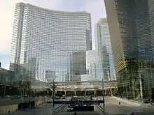 Distant ground-level view of 48-story tower; the building has a curved facade of blue glass. It is under construction, but nearly complete. Several unfinished buildings are visible around it.