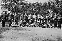 Group photograph of a military band wearing uniforms and holding instruments, some standing and some sitting on the ground