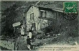 Old postcard with a man and two women wearing aprons in front of a café-restaurant.