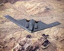 Top view of triangular aircraft, with sawtooth trailing edge, in flight over desert