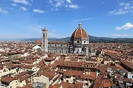 A city with red roofs and a larger domed building in the center.