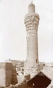 Sepia-toned black-and-white photograph of a much-weathered minaret