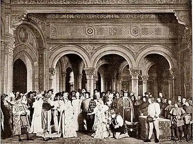 photograph of stage, large cast in 16th century costumes, indoor scene, with young couple bowing to the King of France