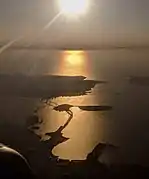 The San Francisco–Oakland Bay Bridge, Yerba Buena Island, Treasure Island, and San Francisco, in an afternoon aerial view looking into the sun