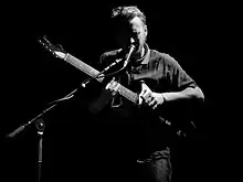 Howard playing an electric guitar while singing into a microphone onstage