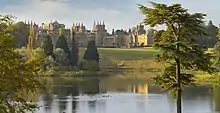 Exterior of a large English Baroque palace fronted by lawns and gardens