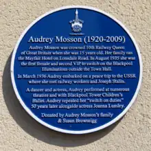 A close up image of the heritage blue plaque dedicated to Audrey Mosson at Lonsdale Avenue. The words read:  Audrey Mosson (1920 -2009) Audrey Mosson was crowned 10th Railway Queen of Great Britain when she was 15 years old. Her family ran the Mayfair Hotel on Lonsdale Road. In August 1935 she was the first female and the second VIP to switch on the Blackpool Illuminations outside the Town Hall.In March 1936 Audrey embarked on a peace trip to the USSR where she met railway workers and Joseph Stalin.A dancer and actress, Audrey performed at numerous theatres and with the Blackpool Tower Children’s Ballet.Audrey repeated her ‘switch-on’ duties 50 years later alongside actress Joanna Lumley. Donated by Audrey Mosson’s family & Susan Brownrigg