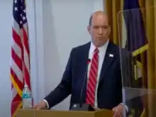 Man at podium with flags of the United States and DuPage County, Illinois in the backgroun