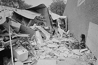 A black and white photograph of a building in ruins next to an intact wall