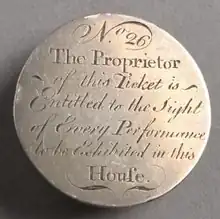 Circular silver token, with engraved writing in a cursive font, with lots of embelishments