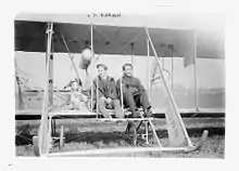 Harry Bingham Brown at the center of an early airplane. On his left sits another passenger.