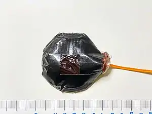 An assembled bullet hit squib device filled with approx. 25 g of fake blood contained in a plastic pouch, secured onto a base with duct tape.