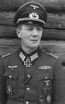 A man wearing a military uniform and peaked cap with an Iron Cross displayed at the front of his uniform collar.