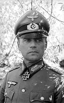 A man wearing a military uniform, peaked cap, and an Iron Cross displayed at the front of his uniform collar.