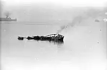 small ship smoke rising and sinking. In the background is a pier