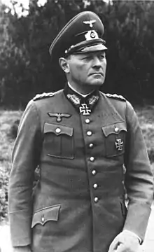 A man wearing a military uniform, peaked cap, and an Iron Cross displayed at the front of his uniform collar.