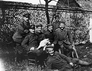 Hitler sitting at far right among soldiers of the "List" regiment and Fuchsl. From left to right, standing: Sperl (Munich), lithographer (?), Max Mund (Munich), gilder; Left to right, sitting: Georg Wimmer (Munich), tram worker, Josef Inkofer (Munich), Lausamer (killed in action), Adolf Hitler; In front: Balthasar Brandmayer (Bad Aibling), bricklayer.