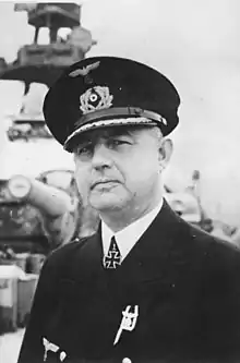 A man wearing a black naval military uniform, peaked cap, and an Iron Cross displayed at the front of his uniform collar.