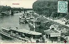 A black and white photograph of a quayside, showing several boats with passengers boarding and disembarking.