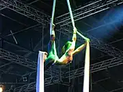 A performer hangs, back arched, between two sheets of tensile fabric.