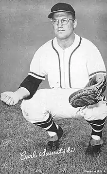 A man in a white baseball uniform squatting in preparation to catch a ball in his mitt.