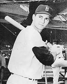 A man in a light baseball uniform and dark undersleeves and cap