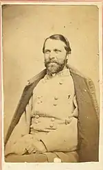 Sepia tone photo of a bearded man wearing a gray military uniform with a cloak draped over his shoulders.