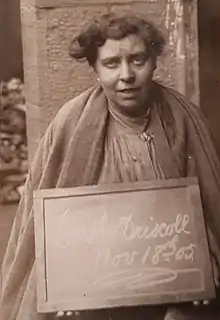 Woman holding a board with "Cath Driscoll Nov 18th 05" written on it in chalk