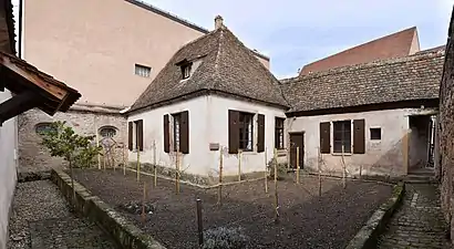 Colour photograph of a small house and garden surrounded by high walls.