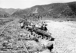 A line of soldiers and tanks hides beneath a berm