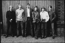 A line-up of 6 young men along an outdoor wall